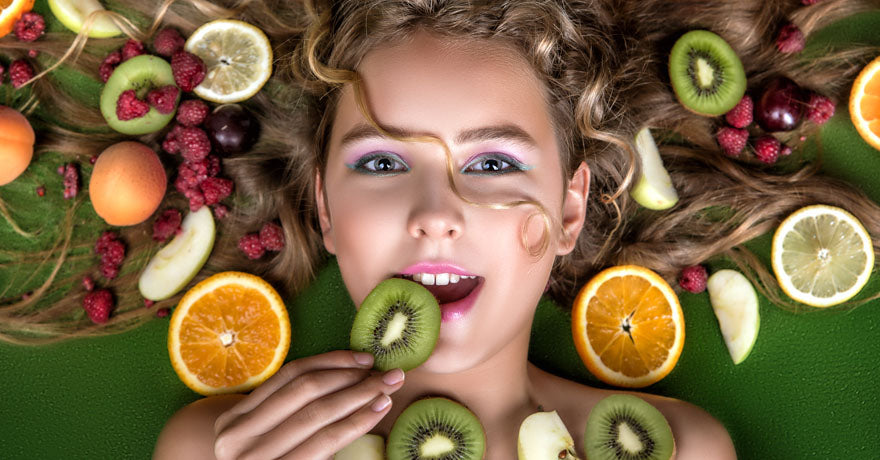 Blond woman with long hair laying on green background with various fruit sliced and placed around her