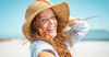 Redheaded woman on beach, holding hat as wind blows her hair