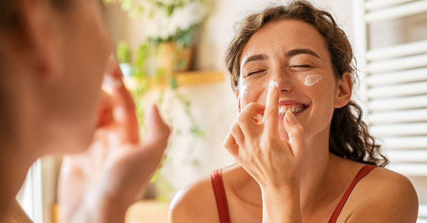 Smiling woman applying face moisturizer in mirror