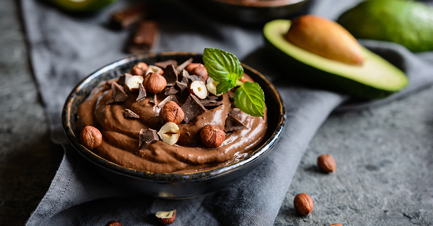 Chocolate mousse in a black bowl, topped with hazelnuts and a mint leaf
