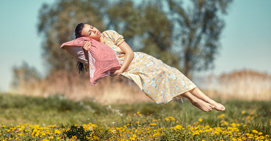 Woman sleeping on pillow, floating mid-air in the meadow