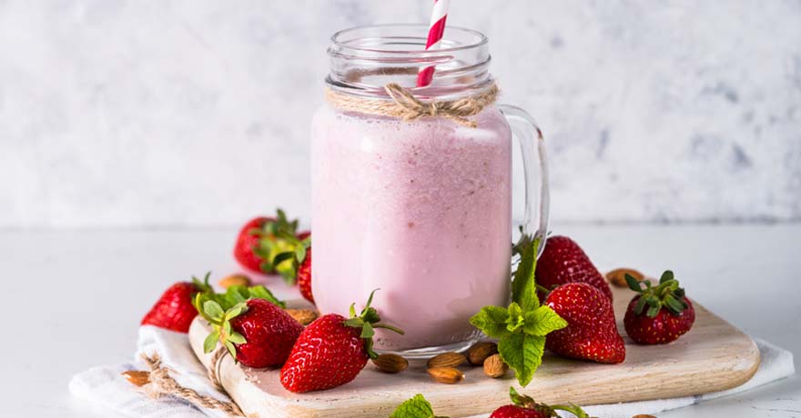 strawberry smoothie in a glass mason jar with strawberries