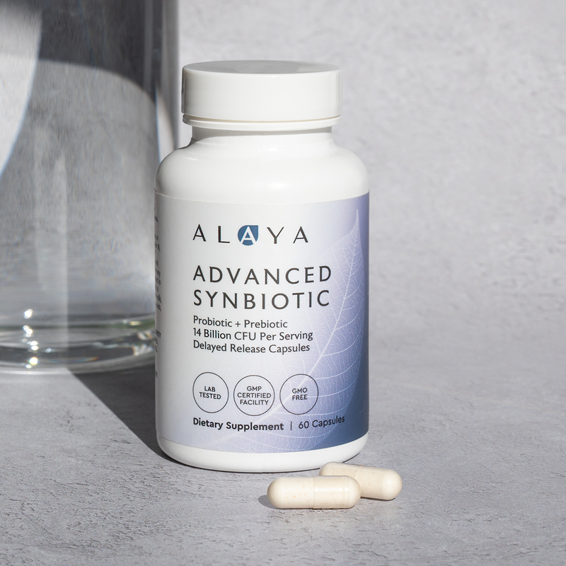 Alaya Advanced Synbiotic supplement bottle on a gray surface with two capsules beside it.